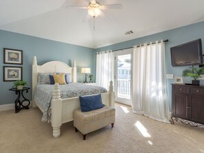 A bedroom with a bed, a ceiling fan, a window with curtains, a television, and a cabinet. - All About Tybee | Quiet Area, Elevator (Tybee Island)