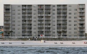 A multi-story hotel with balconies, located near a beach.
