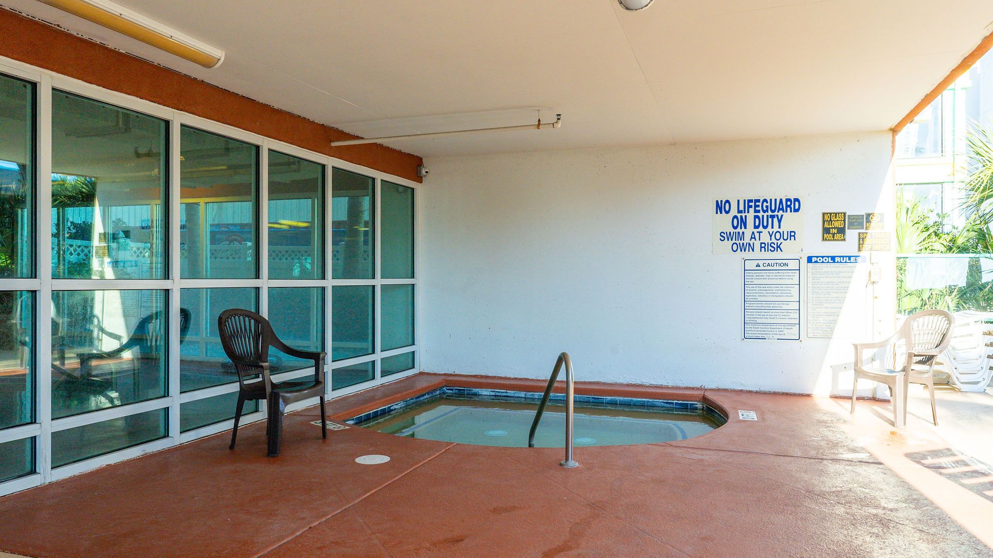 An indoor swimming pool area with a lifeguard sign, chairs, and a pool rules poster.