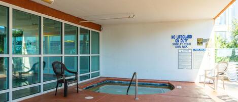 An indoor swimming pool area with a lifeguard sign, chairs, and a pool rules poster.