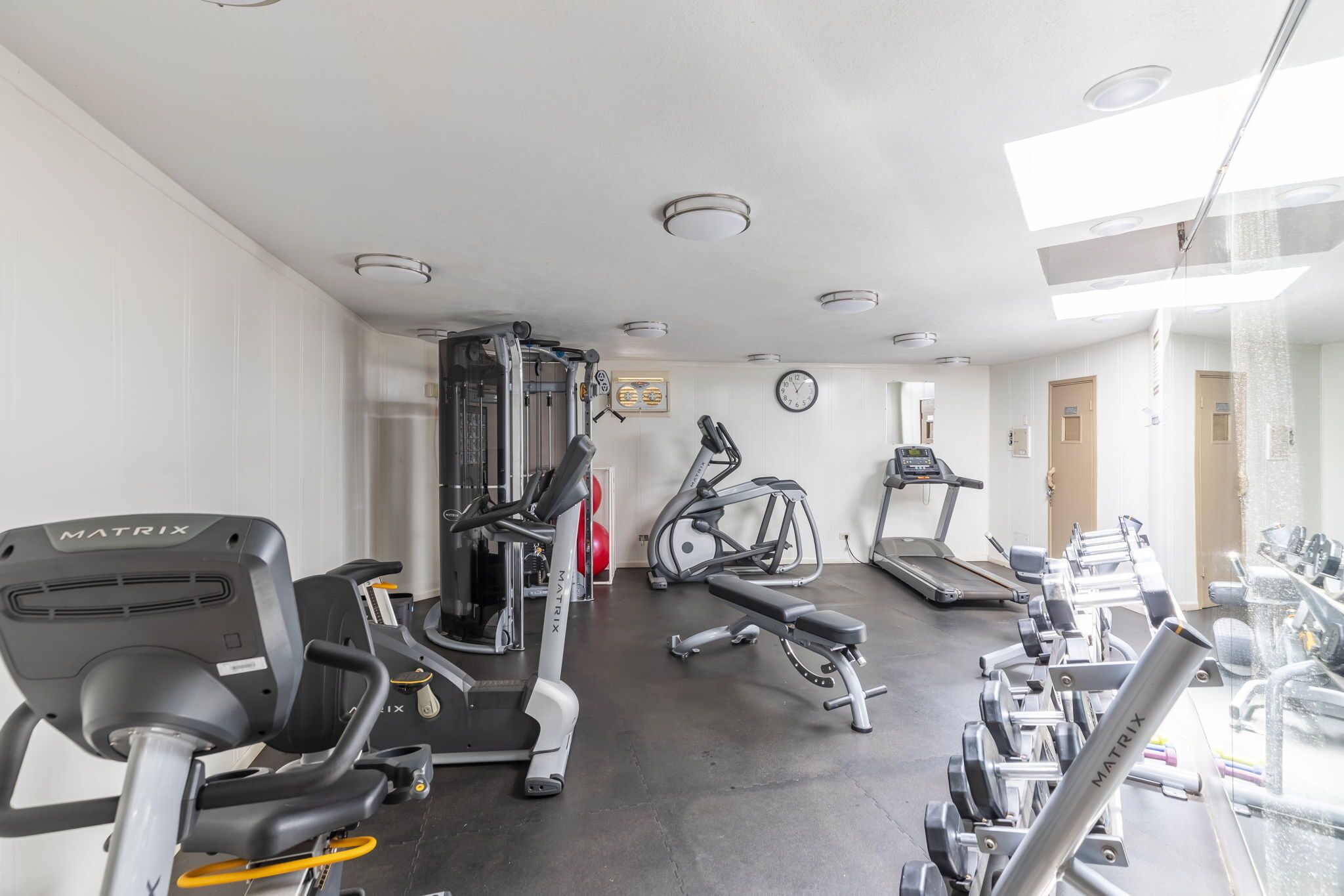 A gym with various exercise equipment, including treadmills and weight machines, and a wall clock.
