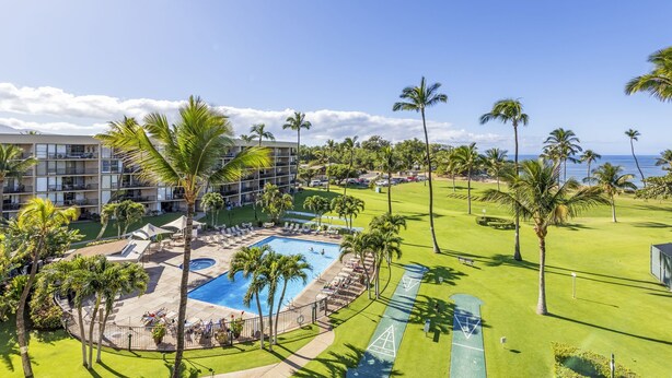 A hotel with a swimming pool, palm trees, and a view of the ocean. - Top floor oceanfront 2 bedroom Maui condo (Kihei)