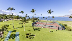 A tennis court surrounded by palm trees and a view of the ocean. - Top floor oceanfront 2 bedroom Maui condo (Kihei)