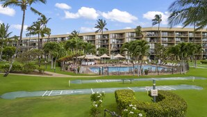 A resort with a swimming pool, palm trees, and a multi-story building with balconies. - Top floor oceanfront 2 bedroom Maui condo (Kihei)