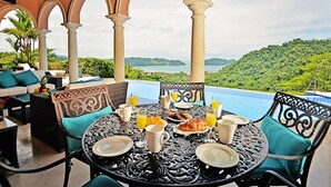 An outdoor dining area with a table set for breakfast, overlooking a scenic view of a lush green landscape and a body of water.