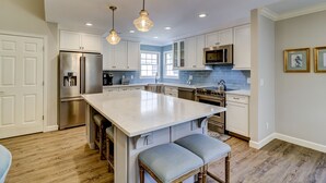 Una cocina moderna con gabinetes blancos, electrodomésticos de acero inoxidable y una isla grande con taburetes de bar.