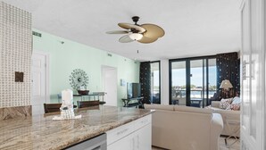 Una cocina moderna con encimera de mármol, muebles de color blanco y un ventilador de techo.
