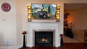 Un salon avec une cheminée, une horloge et un tableau représentant un train.