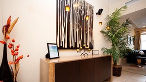 Un espace d’accueil avec un comptoir de réception en bois, un luminaire fixé au mur et une plante en pot.