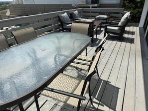 Une terrasse dotée d’une table et de chaises à plateau en verre, entourée d’une autre terrasse en bois et d’une balustrade blanche.