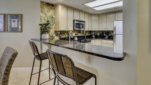 A kitchen with a central island, bar stools, a microwave, a refrigerator, and a backsplash with a leaf pattern. - 6304 Hampton Place- Oceanfront Views, Pool, Spa & So Much More! (Hilton Head Island)