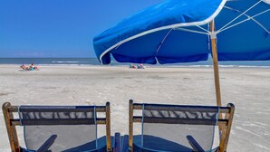 A beach with two blue beach chairs and a blue umbrella. - 6304 Hampton Place- Oceanfront Views, Pool, Spa & So Much More! (Hilton Head Island)