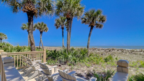 A wooden deck with chairs overlooking a beach with palm trees and a clear sky. - 6304 Hampton Place- Oceanfront Views, Pool, Spa & So Much More! (Hilton Head Island)