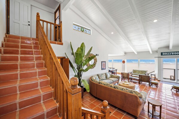 A spacious living area with a curved sofa, wooden staircase, and a large plant.
