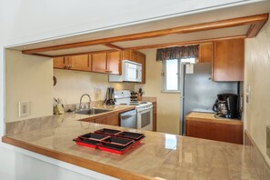 A compact kitchen with wooden cabinets, a microwave, a stove, a sink, and a coffee maker.