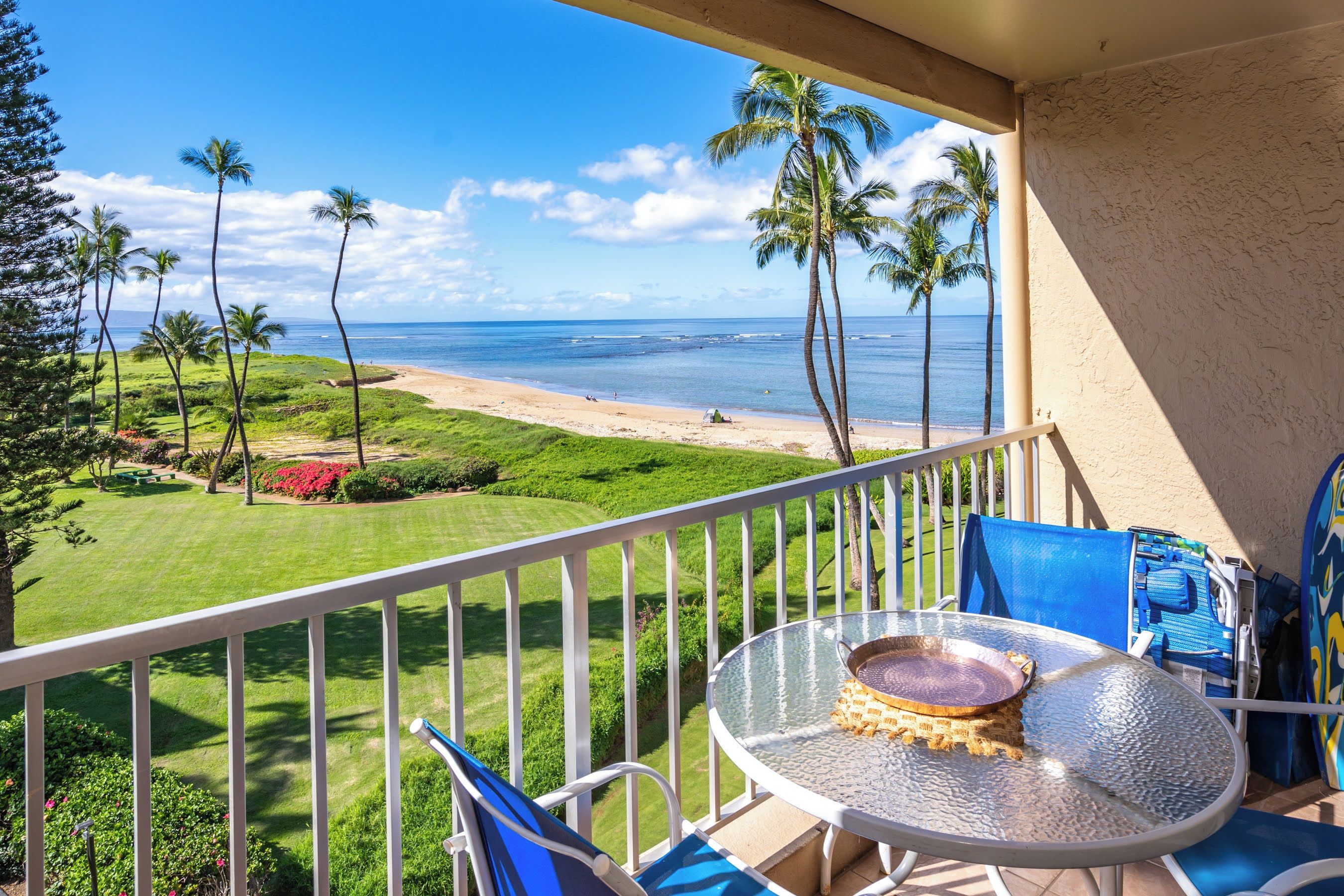 A balcony with a glass table, chairs, and a view of a beach and ocean.