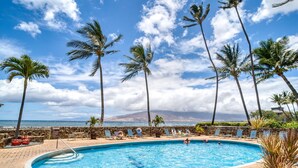 Zona de piscina con sillas de descanso y palmeras, con vista a una playa y al océano.
