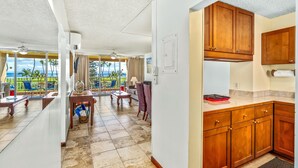 Amplia sala de estar con vista a palmeras y al océano, muebles de madera y una cocina con encimera de mármol.