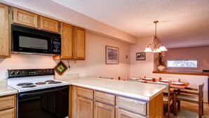 A kitchen with wooden cabinets, a microwave, a stove, and a dining area with a chandelier.