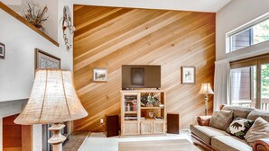 A modern living room with a wooden slat ceiling, a flat-screen TV, a sofa, and a lamp.