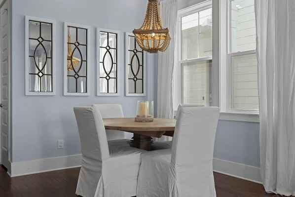 A dining area with a round wooden table, four white upholstered chairs, and three wall-mounted decorative panels. - "Coastal Cottage" at Prominence - 3 Bed / 2.5 BA - Sleeps 8 (Santa Rosa Beach)