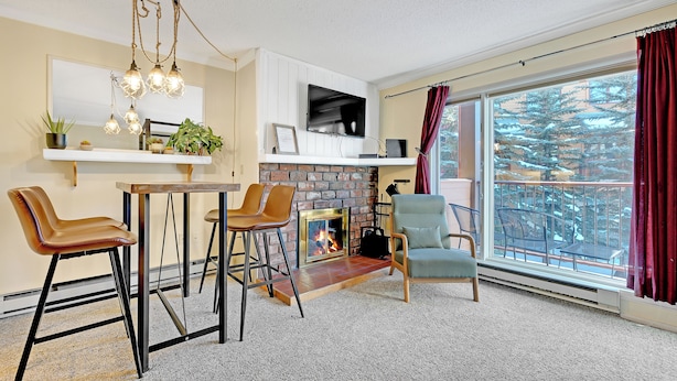 A living room with a fireplace, a TV mounted on the wall, and a large window with curtains. - This Location Can’t Be Beat! Cozy Studio in Downtown Breckenridge l DS109 (Breckenridge)