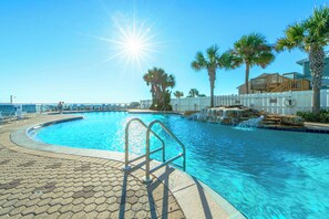 Une piscine baignée de soleil, bordée de palmiers et entourée d’une clôture blanche.