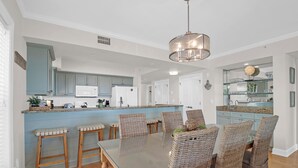Cozinha moderna com ilha central, banquetas e mesa de jantar com cadeiras de vime.