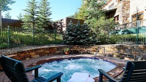 A hot tub surrounded by stone walls and wooden deck chairs, with a stone pathway leading to a building.