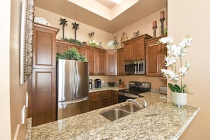 A kitchen with wooden cabinets, stainless steel appliances, granite countertops, and decorative plants. - Lush lobby-level condo w/ private patio (Destin)