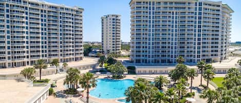 A hotel with multiple high-rise buildings, a central swimming pool, and a landscaped area with palm trees.
