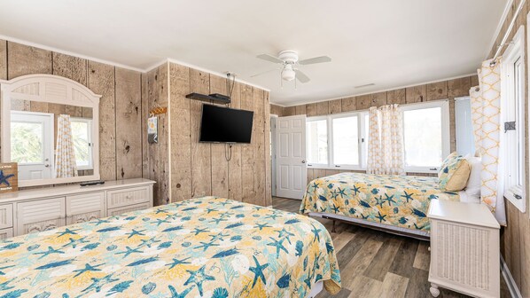Un dormitorio con dos camas, televisión, paredes de madera y ventanas amplias.