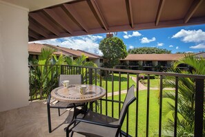 A balcony with a round table and chairs, a view of a well-maintained lawn, and a building in the background.