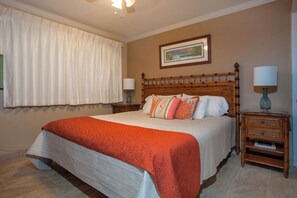 A bedroom with a large bed, two bedside tables, a ceiling fan, a window with curtains, and a framed picture on the wall.