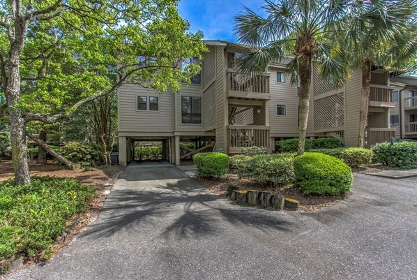A multi-story building with a covered driveway, surrounded by lush greenery and palm trees.
