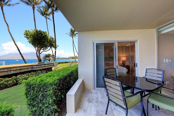A balcony with a glass table and chairs, overlooking a lawn and a view of the ocean.
