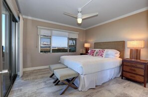 A bedroom with a bed, bench, nightstands, and a ceiling fan.