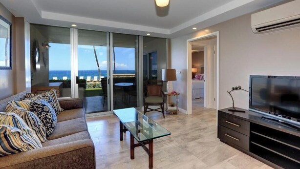Una sala de estar moderna con un sofá, una mesa de centro de vidrio, un televisor y vistas al mar a través de amplios ventanales correderas.