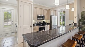 A modern kitchen with white cabinetry, stainless steel appliances, a granite countertop, and bar stools. - ~2 Golf Carts Available*~Pool~Pets Considered, FREE Golf, Bungalo (Miramar Beach)