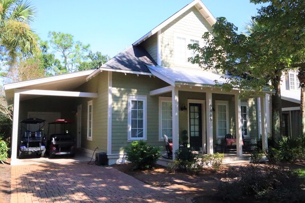 A two-story house with a covered porch, a garage with two golf carts, and a brick driveway.