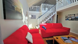 A spacious living area with red sofas, a wooden coffee table, and a staircase with white railings.