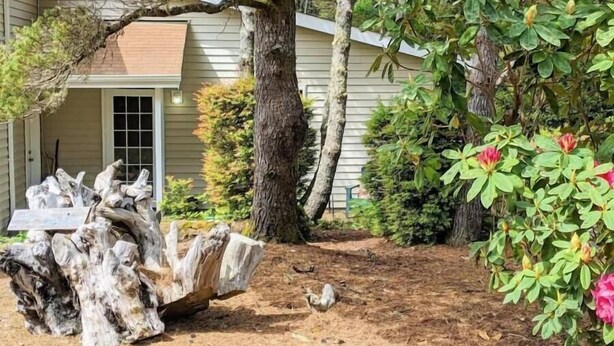A wooden log structure in a garden area with a house in the background. - Surf Sounds Studio – Walk to the Beach, Hear the Waves! (Florence)