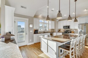 Une cuisine spacieuse avec des meubles blancs, un grand îlot central et des luminaires suspendus.
