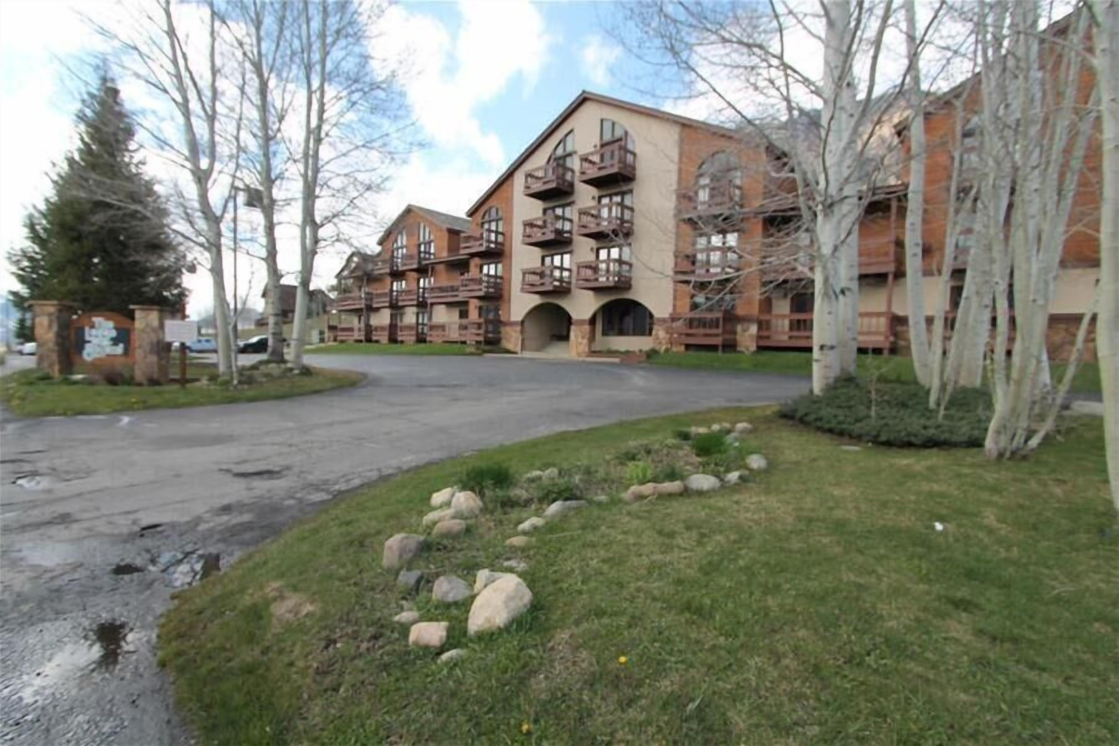 A multi-story building with balconies, a stone entrance, and a grassy area with rocks.