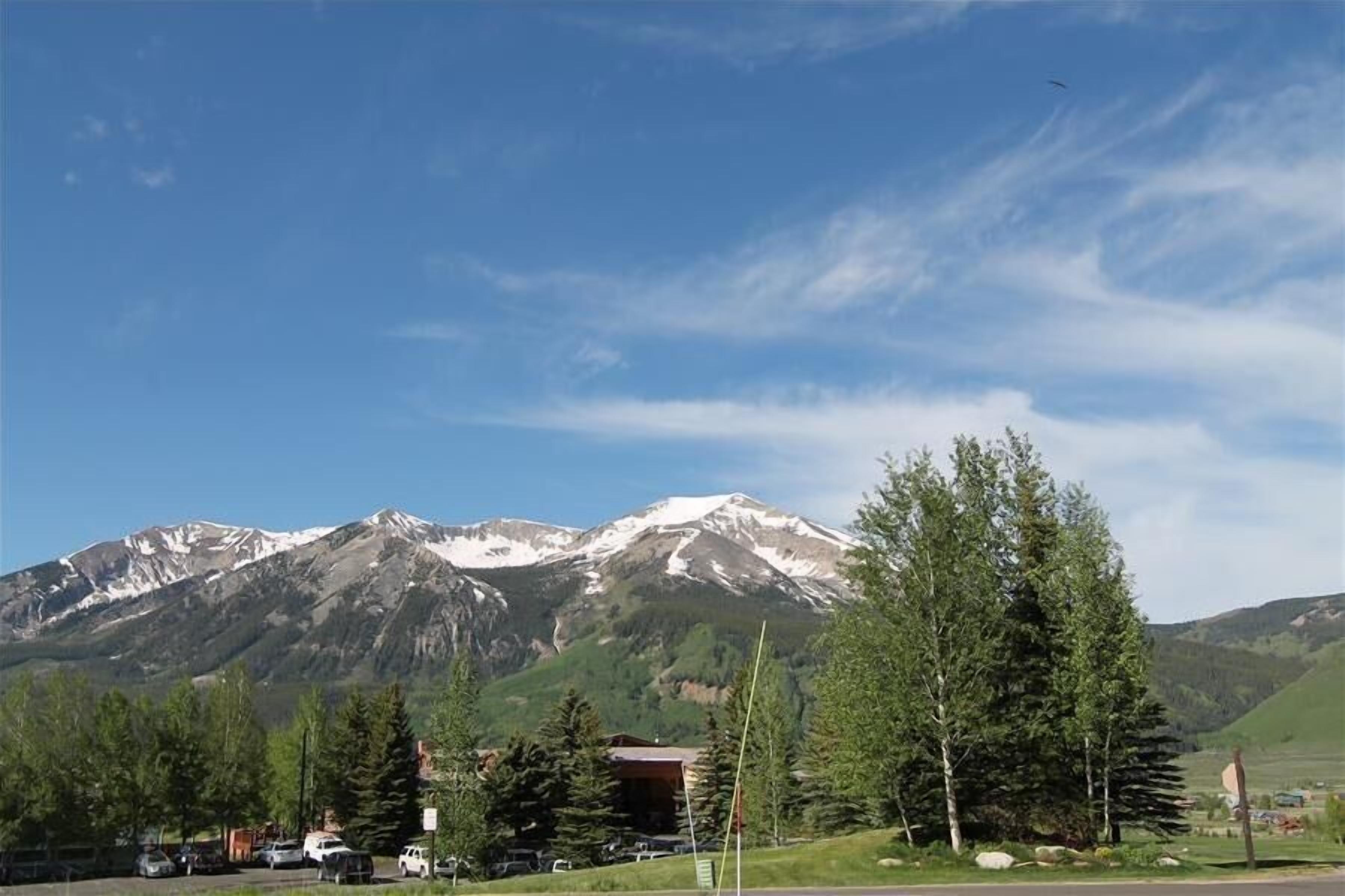 A mountain landscape with a clear sky, a parking area with vehicles, and a building with a red roof.