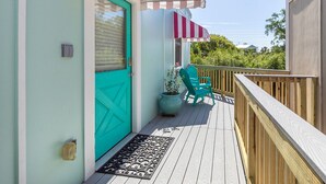 Une terrasse en bois avec une porte turquoise, une plante en pot et une chaise.
