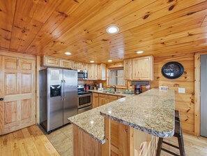 A kitchen with wooden cabinets, a stainless steel refrigerator, a microwave, and a granite countertop. - Secluded | Pigeon Forge | Pool Table | Arcade | Pet Friendly | Hot Tub | WiFi (PIGEON FORGE)