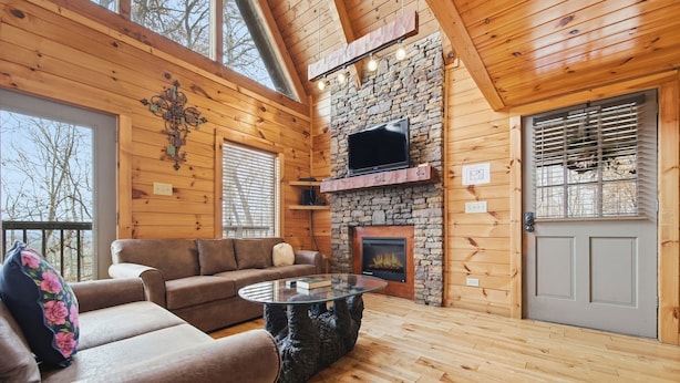 A cozy cabin interior with a stone fireplace, wooden walls, a sofa, and a television.