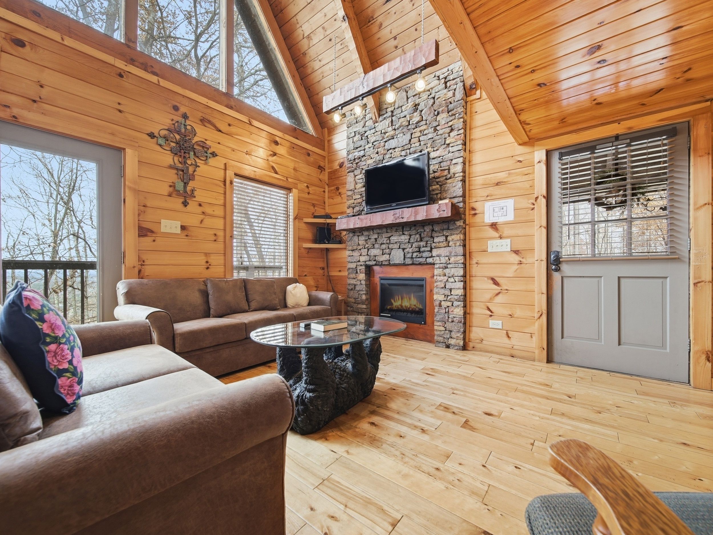 A cozy cabin interior with a stone fireplace, wooden walls, a sofa, and a television.