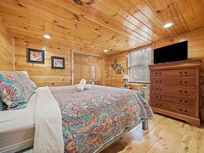 A wooden cabin bedroom with a bed, dresser, and a television. - Secluded | Pigeon Forge | Pool Table | Arcade | Pet Friendly | Hot Tub | WiFi (PIGEON FORGE)